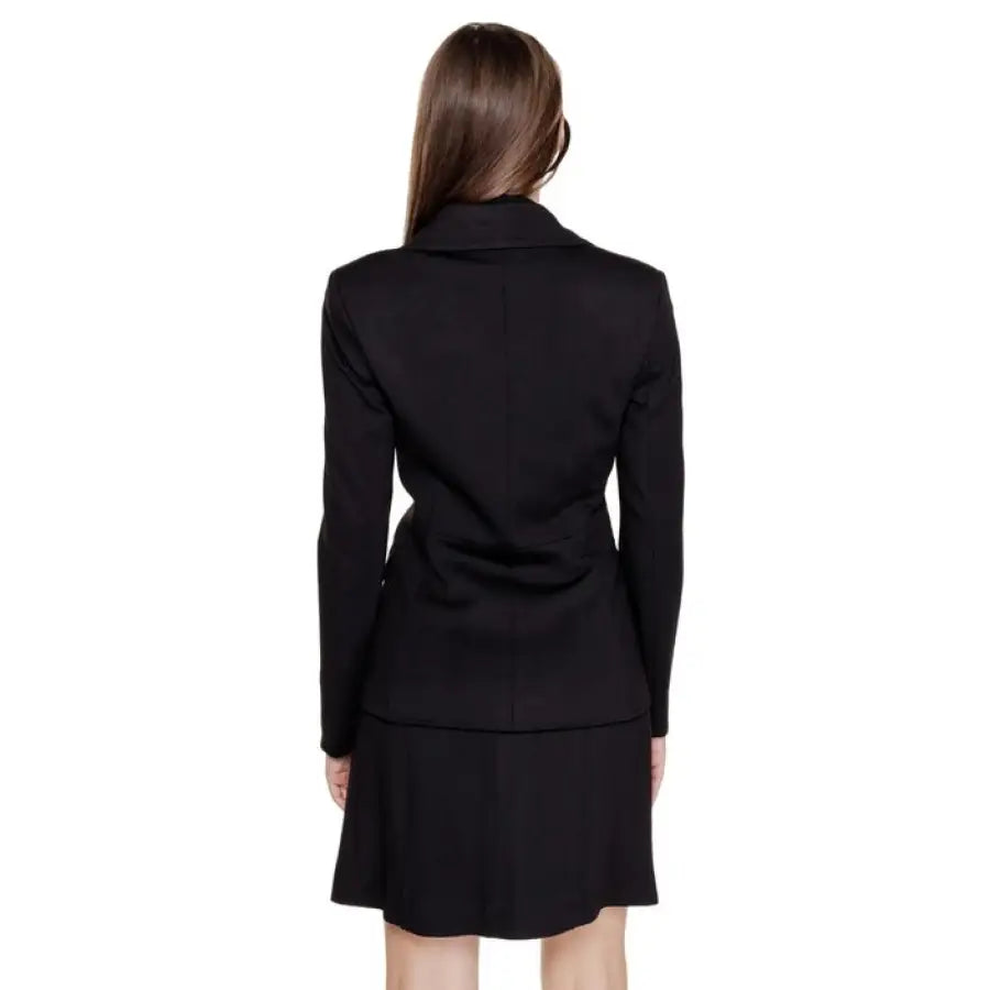 Woman with long brown hair wearing Guess black blazer, viewed from behind