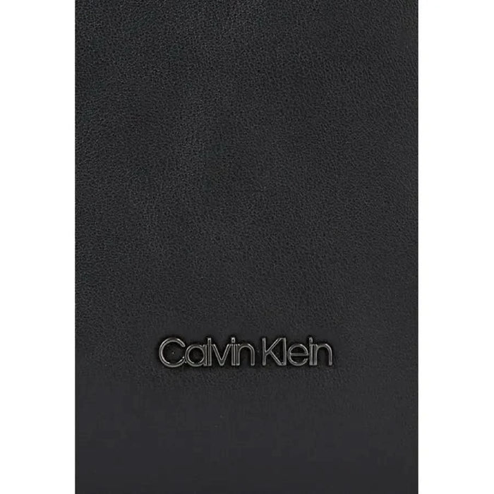 Black leather surface featuring embossed Calvin Klein logo on a men’s bag