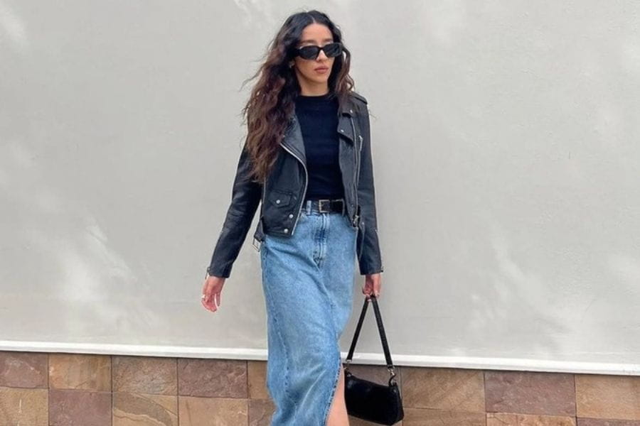 Long denim skirt styled with a black leather jacket and trendy sunglasses.