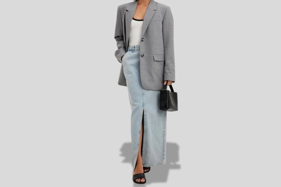 Long denim skirt with front slit styled with gray blazer and black accessories.