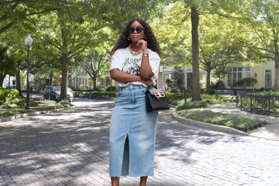 Long denim skirt with front slit styled with patterned white top and stylish sunglasses.