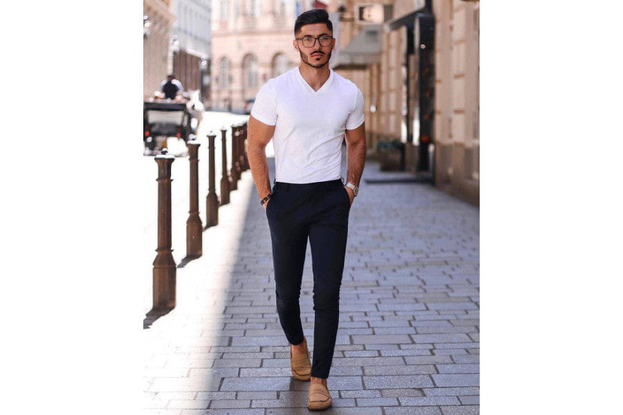 Man in a white t-shirt and dark pants walking on a cobblestone street, showcasing minimalist outfits.