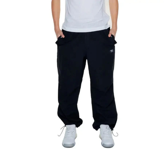 Karl Kani urban style clothing: man in white shirt and black Karl Kani Men Trousers