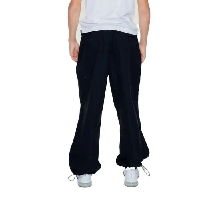 A man in a white shirt and black Karl Kani Men Trousers showcasing urban style clothing