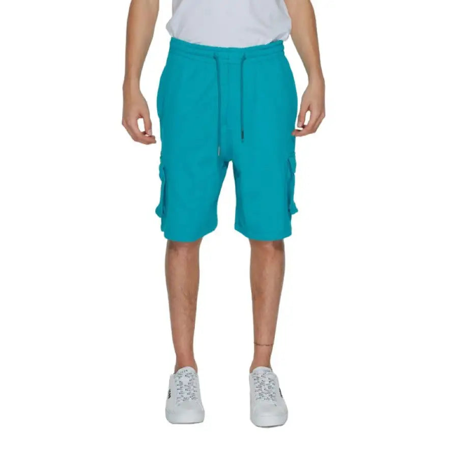 Man wearing white t-shirt and turquoise ’Pharmacy - Pharmacy Men Shorts’ in a stylish pose