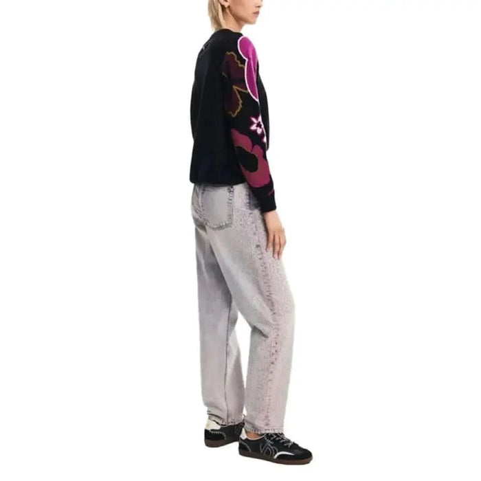 Person in black Desigual sweater with pink and purple designs and light gray pants