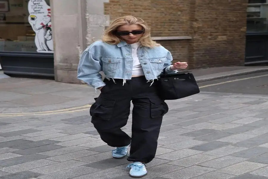 Person in cropped denim jacket, baggy black cargo pants, and blue sneakers for stylish look.