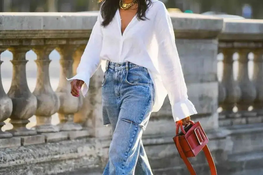 Person in white oversized shirt and blue jeans with a red handbag for trendy style.