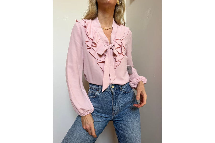 Pink ruffled blouse with long sleeves and tie-front detail showcasing trendy 70s fashion style.