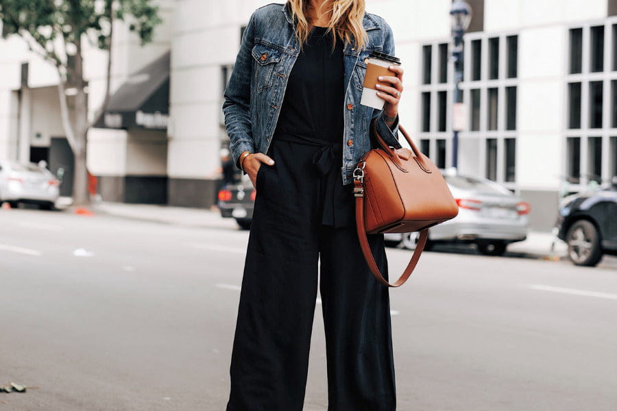 Stylish black jumpsuit with denim jacket and brown leather handbag ensemble.