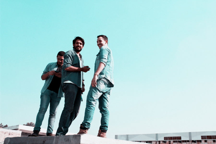 Three individuals on a concrete ledge against a blue sky, showcasing denim jacket styles.