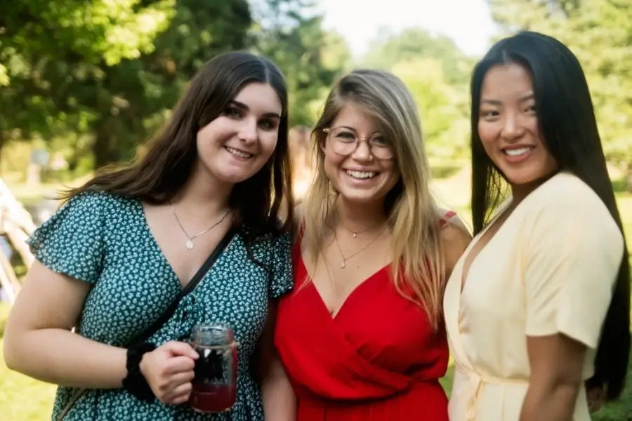 Three smiling young women enjoying the outdoors in stylish wedding guest attire.