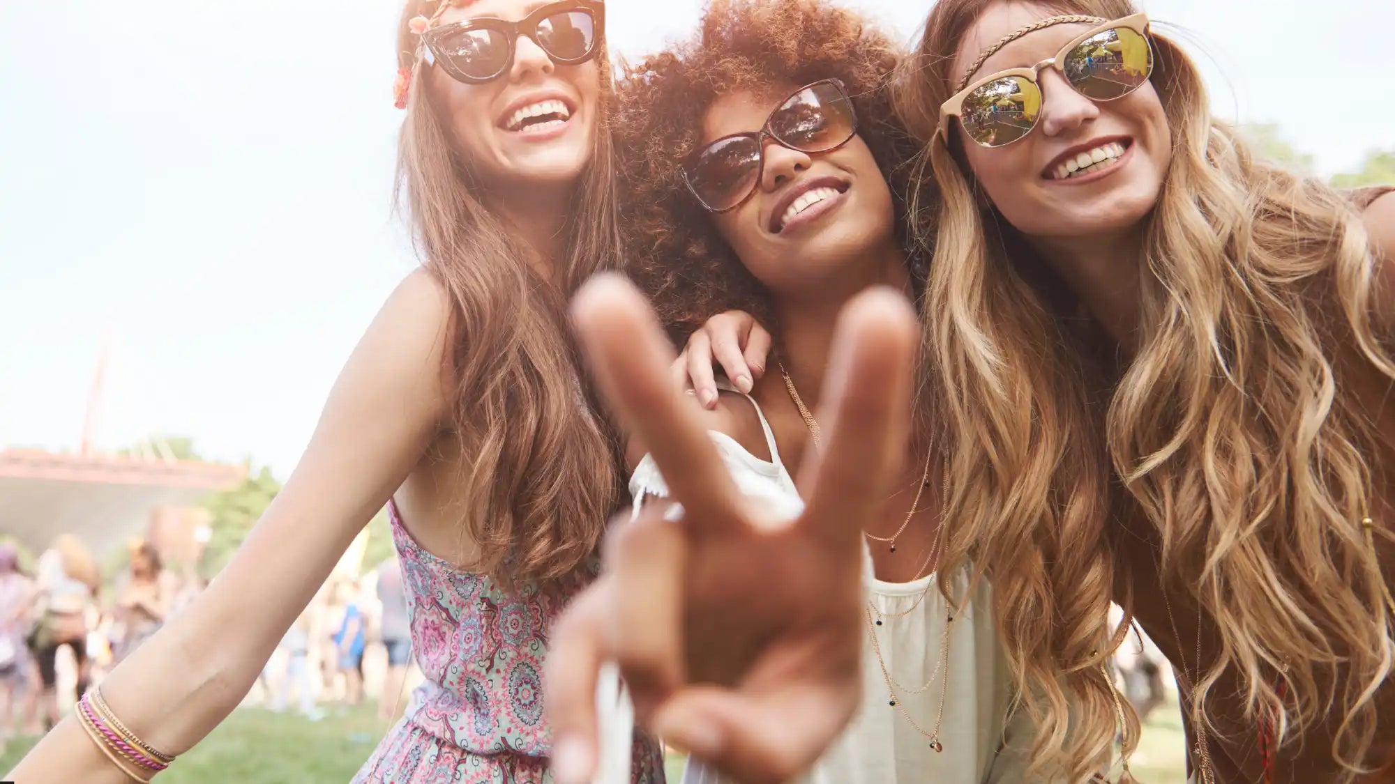 Three smiling young women wearing sunglasses and summer clothing.