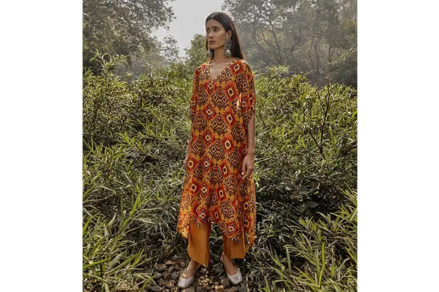 Vibrant orange and red floral dress showcasing 70s trend, featuring long sleeves and asymmetrical hemline.