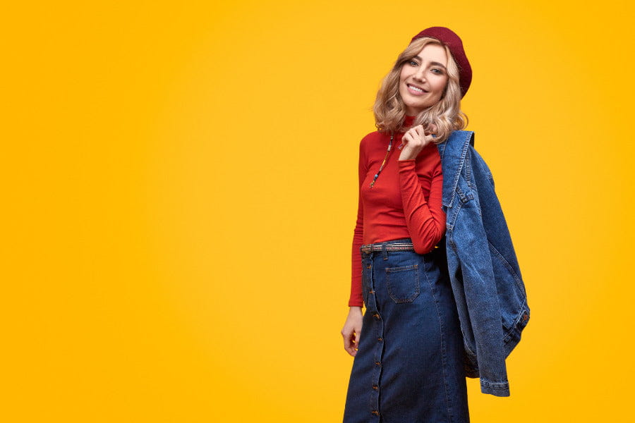 Person in a red sweater, denim jacket, jeans, and burgundy beanie in casual pose.