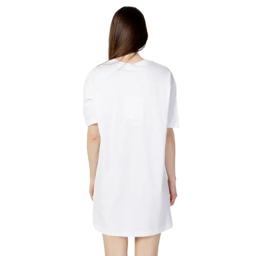 Person with long brown hair wearing Love Moschino white oversized t-shirt dress from behind