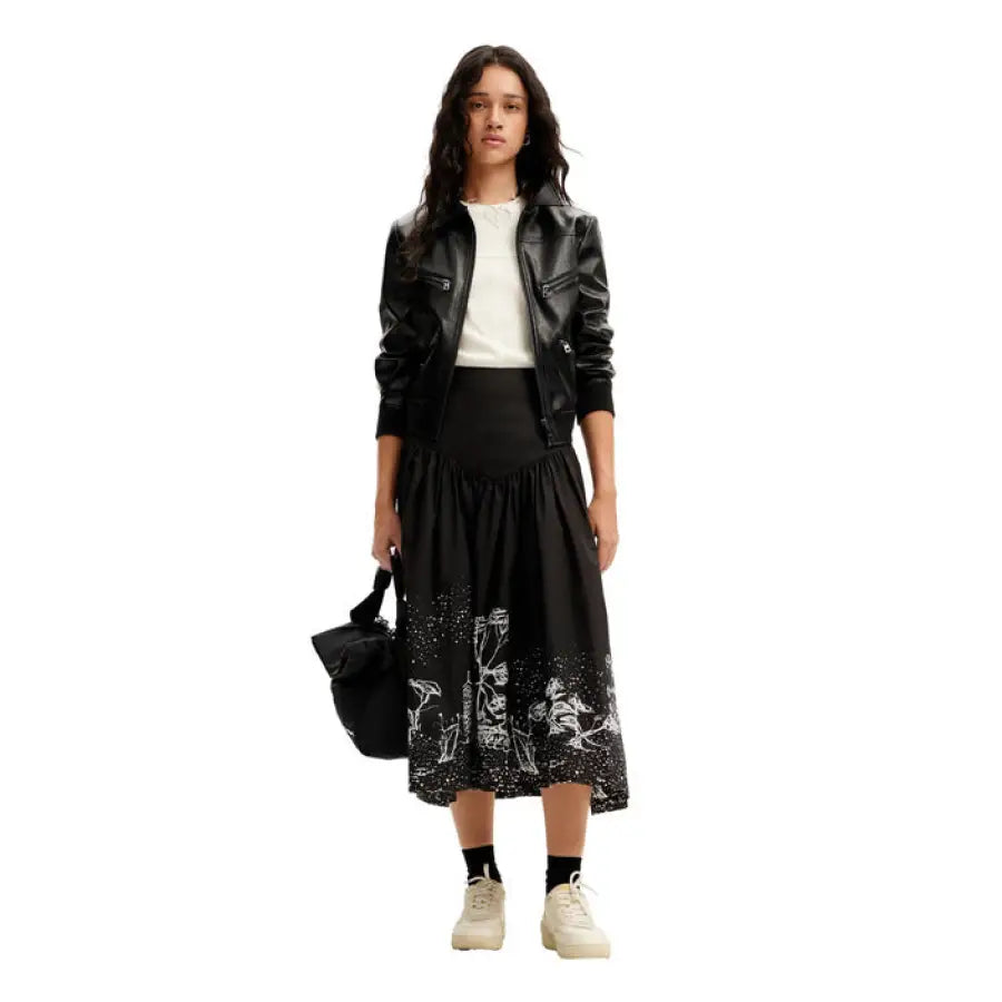Woman in stylish Desigual outfit: black leather jacket, white top, patterned skirt, white sneakers