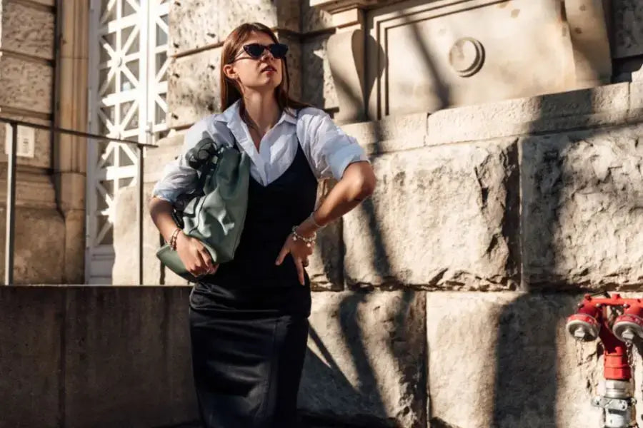 Woman in business attire with oversized shirt leaning against a stone wall.