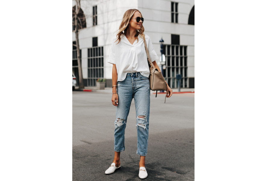 Woman in a minimalist outfit with a white shirt, ripped jeans, and white sneakers.