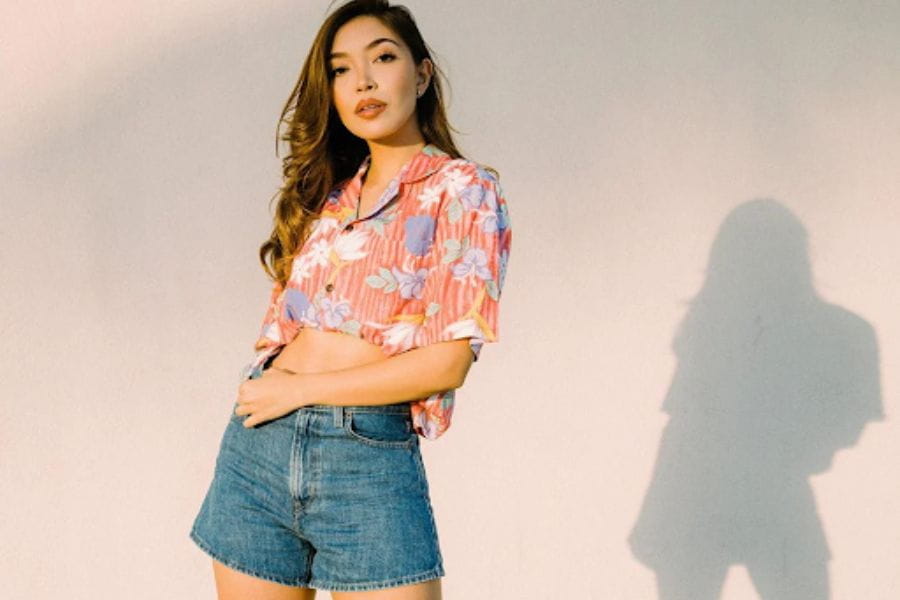 Woman in colorful floral shirt and denim shorts showcasing holiday outfit ideas.