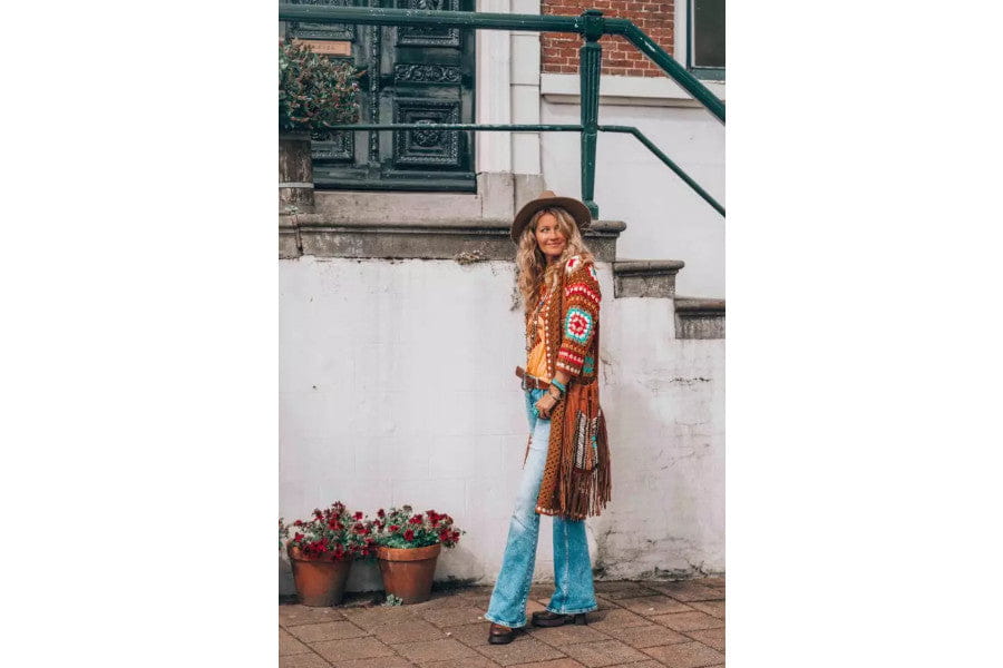 Woman in colorful patterned cardigan and flared jeans showcasing 70s fashion trends.