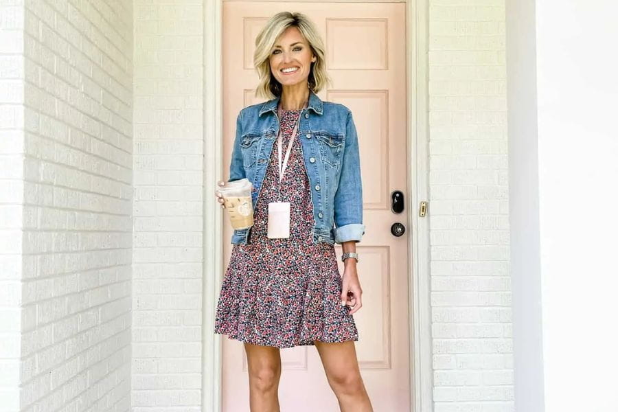 Woman in a floral dress and denim jacket showcasing chic summer work outfits at doorway.