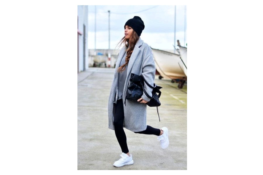 Woman in a long gray coat and black hat showcasing stylish minimalist outfits to shop.