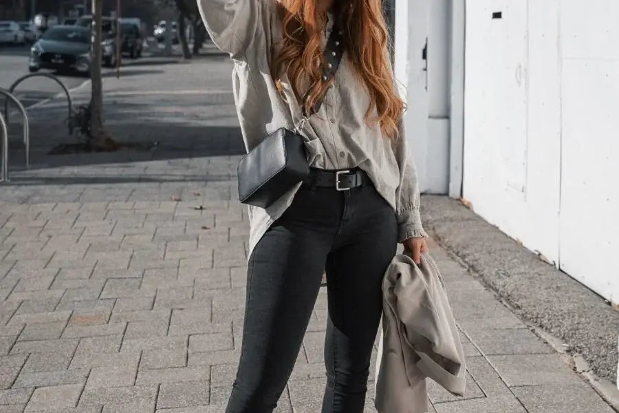 Woman in stylish outfit featuring oversized shirt, black pants, and handbag on city sidewalk.