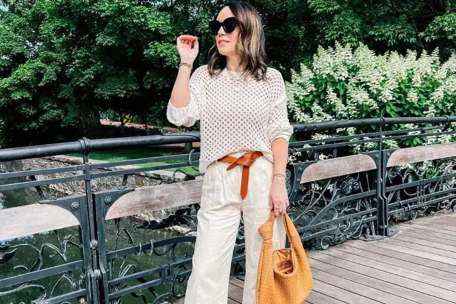 Woman in sunglasses and polka dot top showcasing summer work outfits on a bridge.