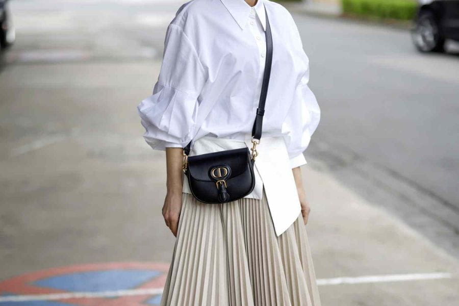 Woman in a white blouse and pleated skirt showcasing stylish oversized shirts.