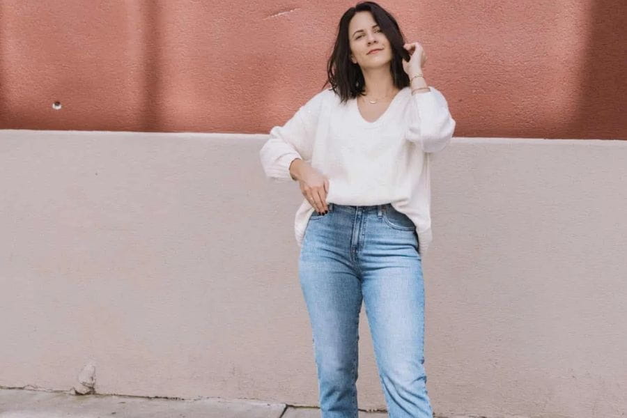 Woman in a white sweater and blue jeans showcasing summer work outfits for the office.