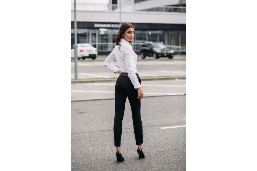 Woman in white shirt and black pants showcasing minimalist apparel on city street.