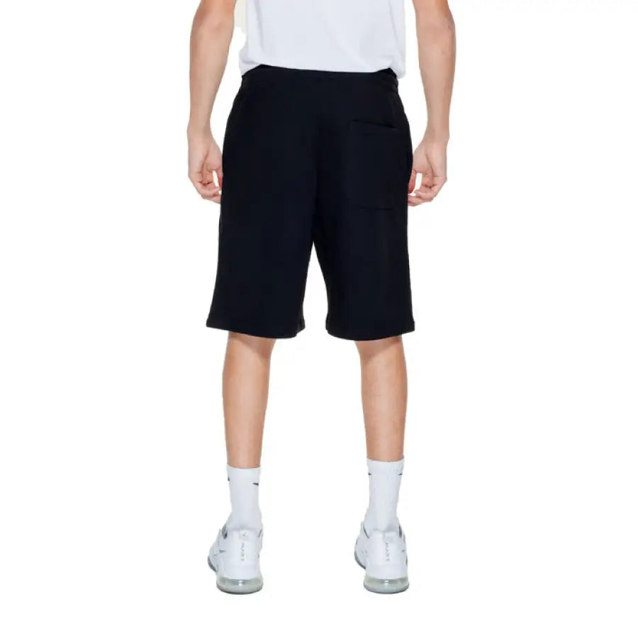 Young boy in white T-shirt and black Pharmacy Men Shorts standing outdoors